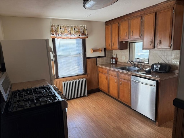 kitchen featuring radiator heating unit, stainless steel dishwasher, freestanding refrigerator, black range with gas cooktop, and a sink