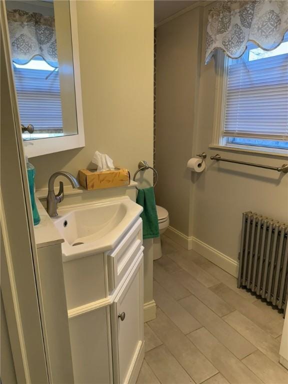 bathroom with toilet, wood finished floors, radiator heating unit, baseboards, and vanity