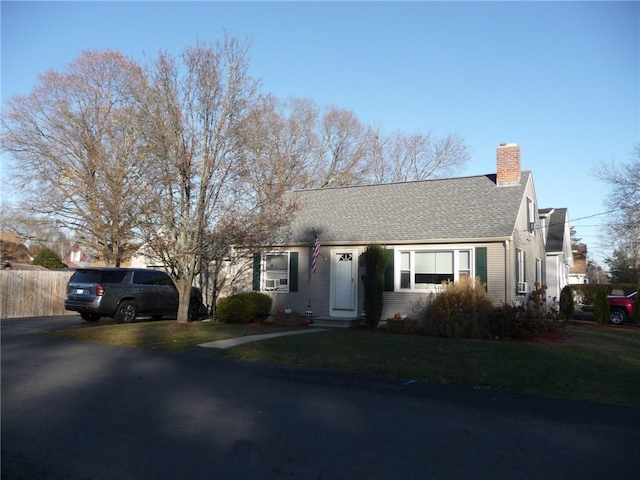 view of front of house with fence, a chimney, a front yard, and a shingled roof