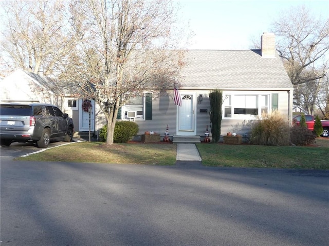 view of front of home featuring a front lawn, cooling unit, a chimney, and a shingled roof