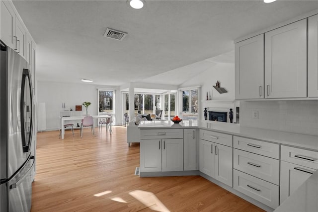 kitchen with visible vents, light wood finished floors, a peninsula, freestanding refrigerator, and open floor plan