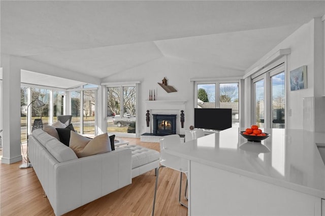 living area with a glass covered fireplace, lofted ceiling, and light wood-style floors