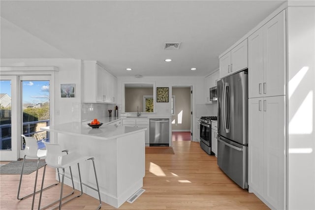 kitchen with visible vents, a peninsula, a sink, stainless steel appliances, and a kitchen breakfast bar