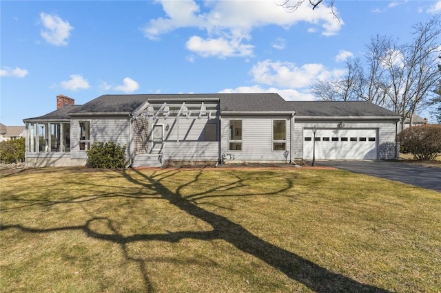 view of front of house with an attached garage, a chimney, driveway, and a front yard