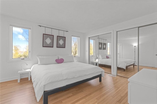 bedroom featuring multiple windows, multiple closets, baseboards, and light wood finished floors