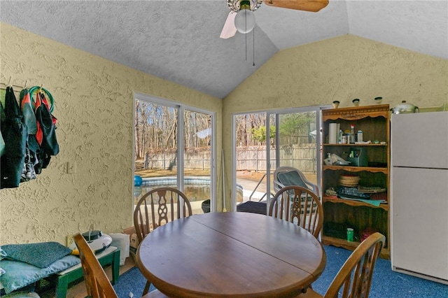 dining space with a textured ceiling, carpet floors, ceiling fan, vaulted ceiling, and a textured wall