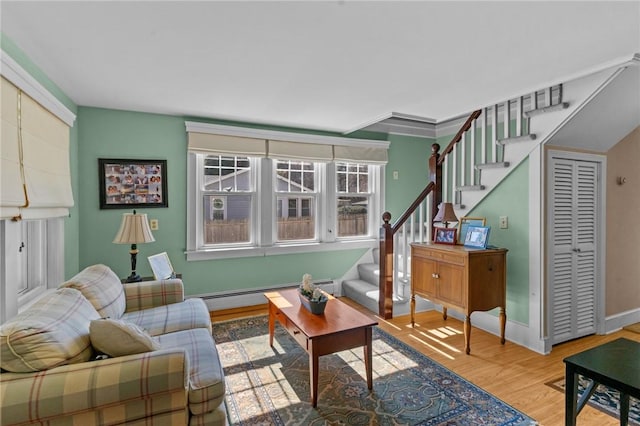 living room with wood finished floors, baseboards, a baseboard radiator, ornamental molding, and stairs