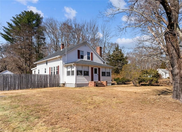 view of front facade with entry steps, a front lawn, fence, and a chimney