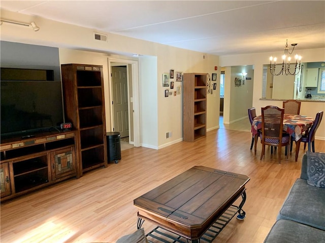 living room featuring visible vents, baseboards, light wood-style floors, and a notable chandelier