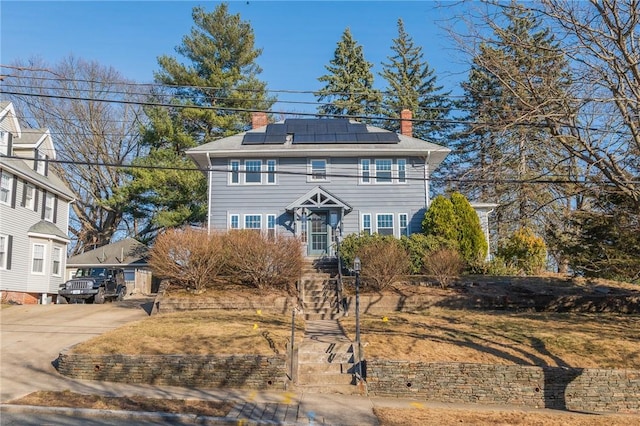 view of front of house with a chimney, solar panels, and driveway