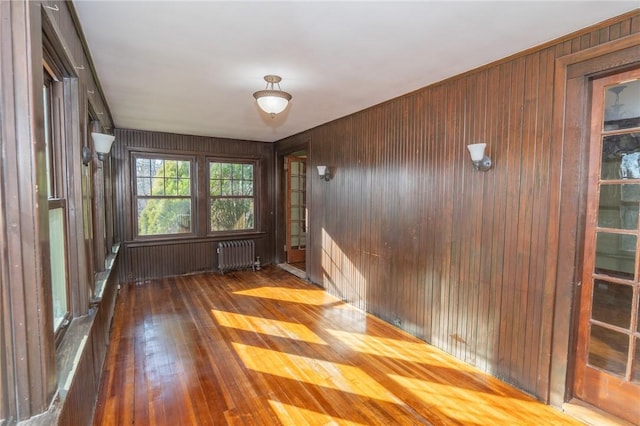 unfurnished room featuring hardwood / wood-style flooring, wooden walls, and radiator heating unit