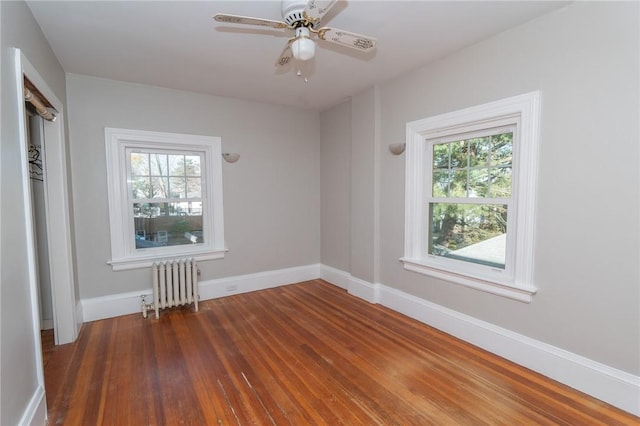 empty room with ceiling fan, baseboards, wood finished floors, and radiator heating unit