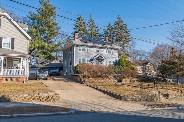 view of front of house featuring an outbuilding, covered porch, concrete driveway, and a chimney