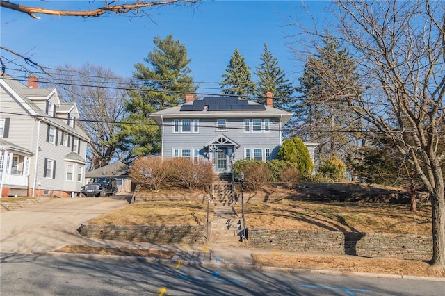 view of front of property with roof mounted solar panels, concrete driveway, and a chimney