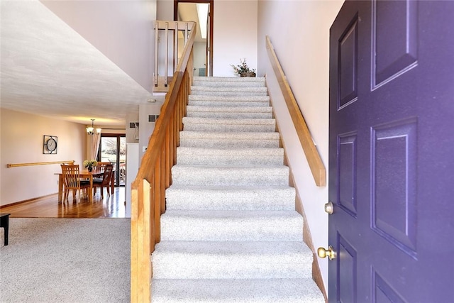 stairway with a notable chandelier and carpet flooring