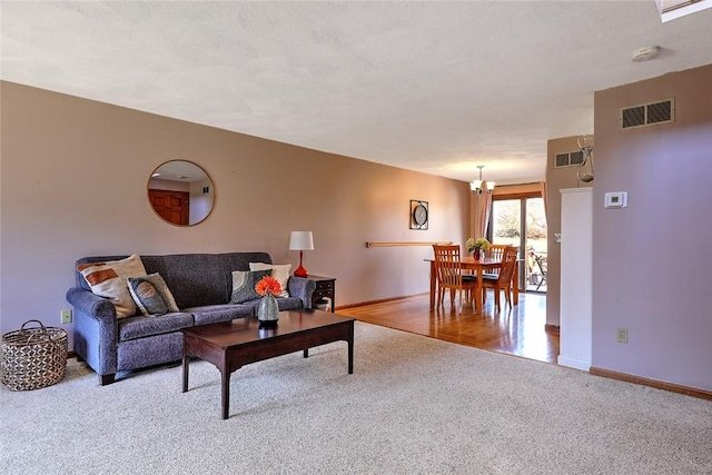 carpeted living room featuring visible vents, baseboards, a textured ceiling, and a chandelier