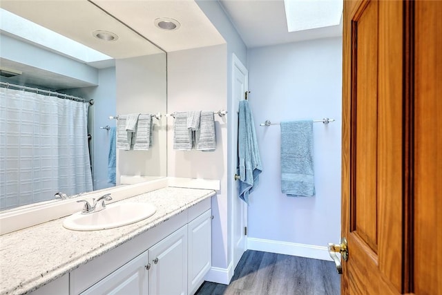 bathroom featuring wood finished floors, a shower with shower curtain, a skylight, baseboards, and vanity