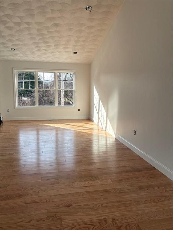 spare room featuring vaulted ceiling, wood finished floors, and baseboards