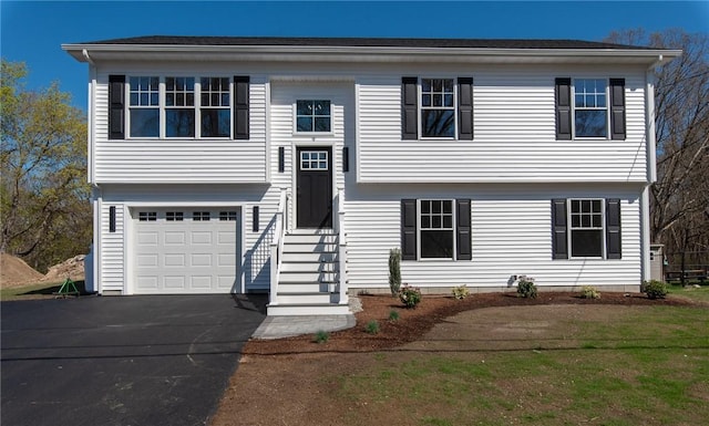 raised ranch with entry steps, aphalt driveway, and an attached garage