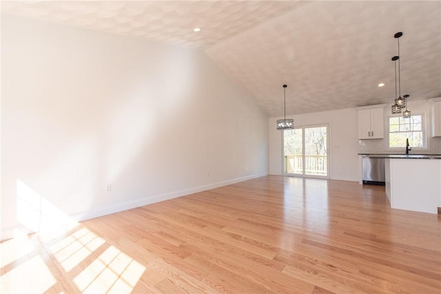 unfurnished living room featuring lofted ceiling, recessed lighting, light wood finished floors, and a notable chandelier
