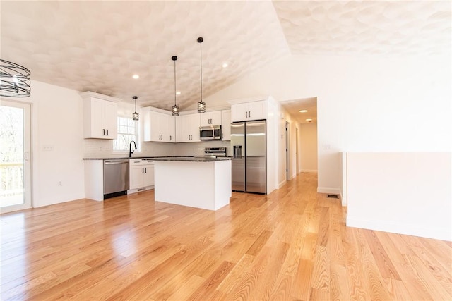 kitchen with a center island, dark countertops, light wood finished floors, and appliances with stainless steel finishes