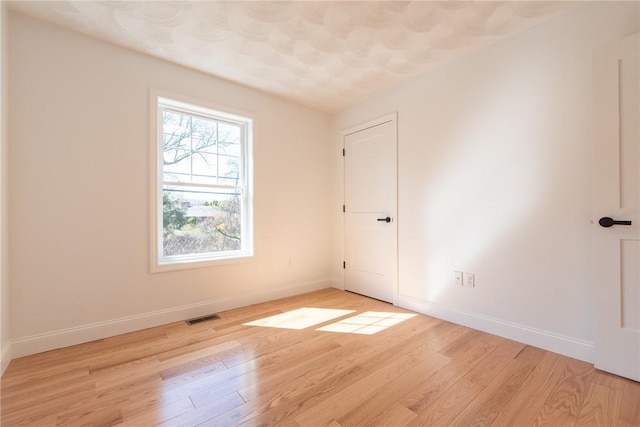 empty room with light wood finished floors, visible vents, and baseboards