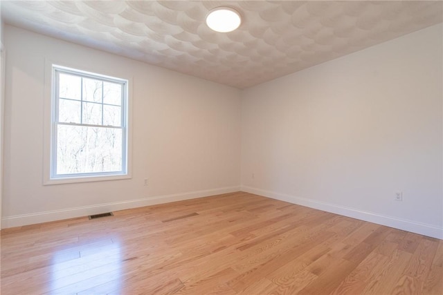 empty room featuring baseboards, visible vents, a healthy amount of sunlight, and light wood-style flooring