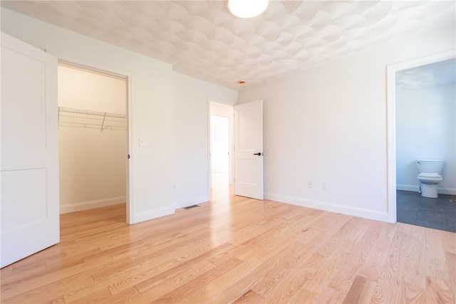unfurnished bedroom with light wood-style floors, a spacious closet, baseboards, and a closet