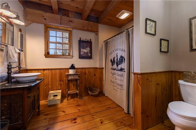 full bathroom featuring beamed ceiling, toilet, wood walls, and wainscoting