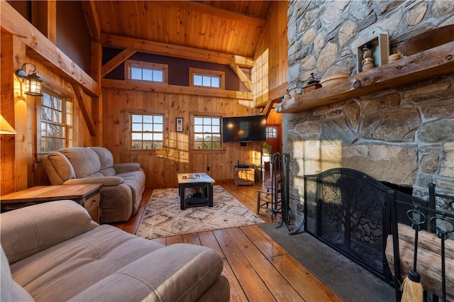 living room with beam ceiling, wood-type flooring, wooden walls, a stone fireplace, and wood ceiling