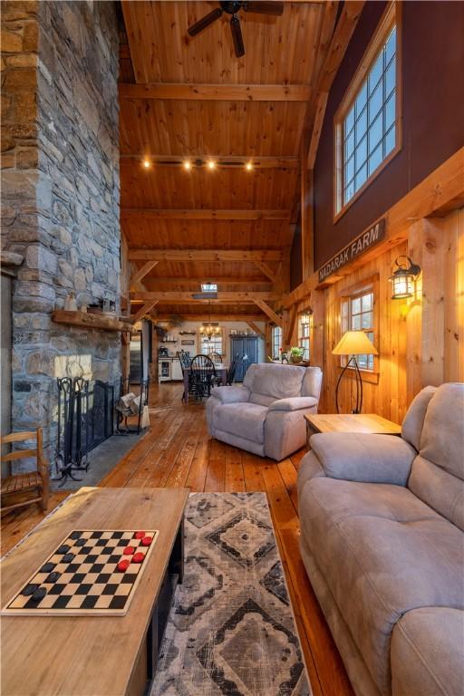 living area with a ceiling fan, high vaulted ceiling, a stone fireplace, wood ceiling, and wood-type flooring