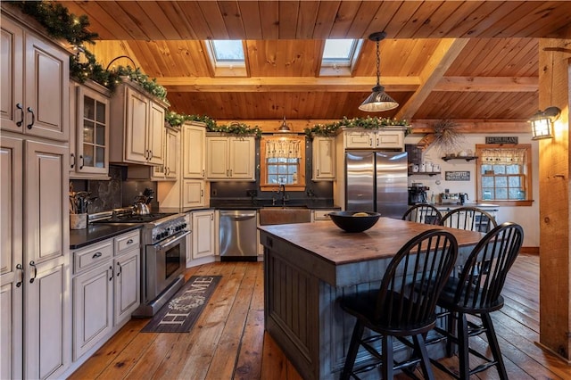 kitchen with beam ceiling, light wood-style flooring, a skylight, stainless steel appliances, and wood counters