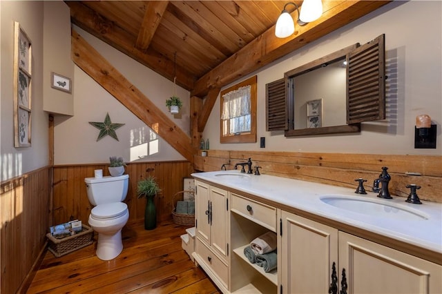 bathroom featuring a wainscoted wall, toilet, wooden walls, and a sink