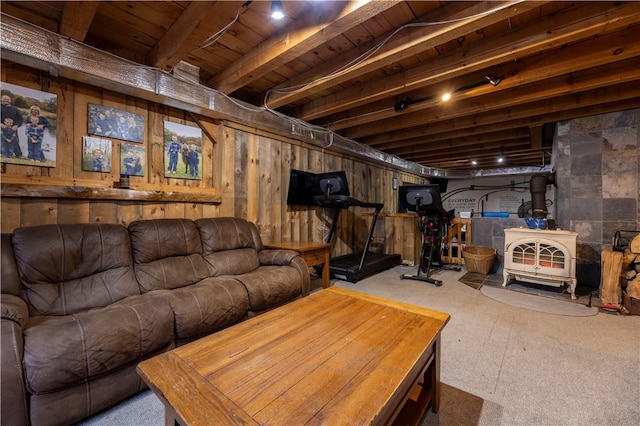 living area featuring beam ceiling, wooden walls, and a wood stove