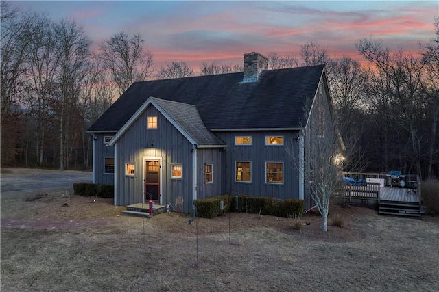 view of front facade with board and batten siding, a chimney, a deck, and a shingled roof