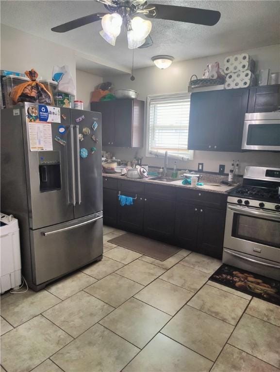 kitchen with a ceiling fan, a sink, a textured ceiling, stainless steel appliances, and light tile patterned floors