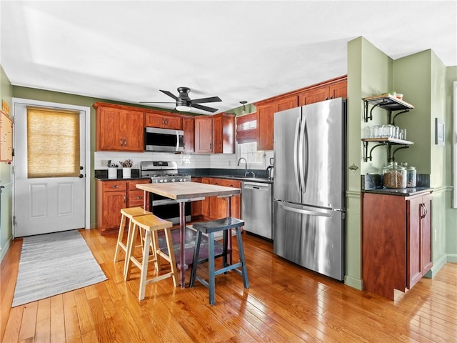 kitchen with dark countertops, backsplash, appliances with stainless steel finishes, light wood-style floors, and open shelves