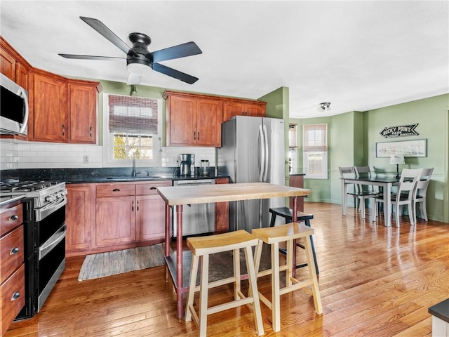 kitchen featuring a sink, light wood-style floors, appliances with stainless steel finishes, dark countertops, and tasteful backsplash