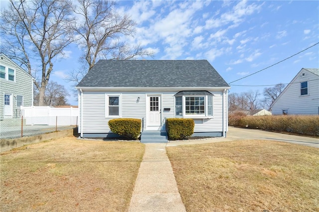 view of front facade with a front yard, fence, and a shingled roof