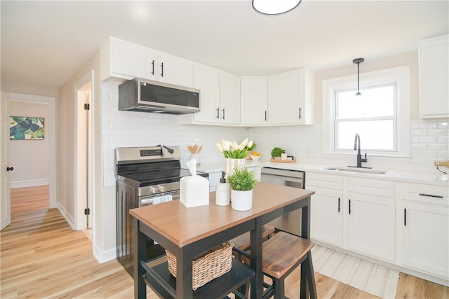 kitchen featuring white cabinets, stainless steel appliances, light wood-style flooring, and a sink