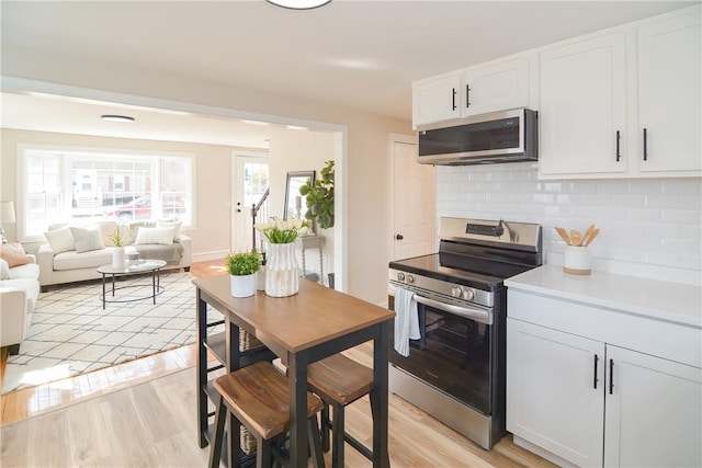 kitchen with white cabinetry, backsplash, light wood-type flooring, and appliances with stainless steel finishes