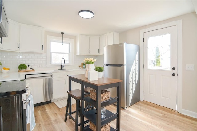 kitchen with a sink, stainless steel appliances, light wood-style floors, and decorative backsplash