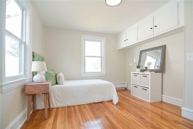 bedroom featuring light wood finished floors, baseboard heating, multiple windows, and baseboards