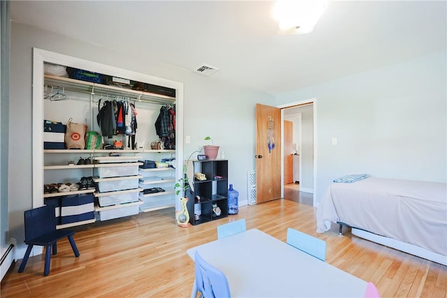 bedroom with visible vents, baseboards, baseboard heating, wood finished floors, and a closet