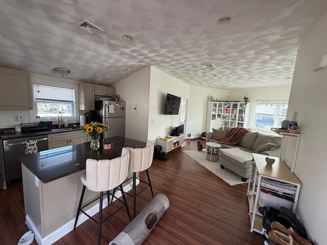 kitchen with visible vents, a breakfast bar, a sink, dark countertops, and appliances with stainless steel finishes