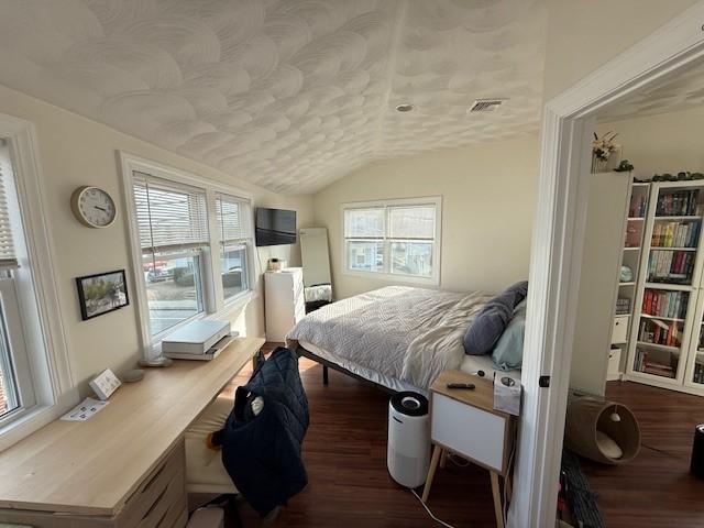 bedroom with visible vents, multiple windows, lofted ceiling, and wood finished floors