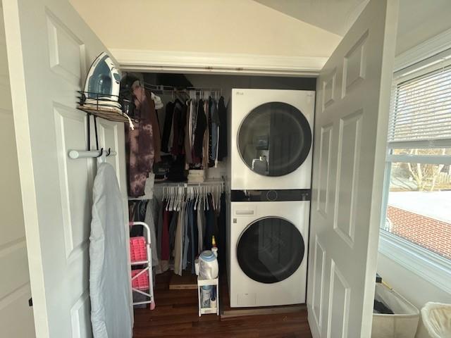 laundry room with dark wood-type flooring, stacked washer and clothes dryer, and laundry area