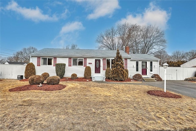 single story home featuring aphalt driveway, a chimney, a front lawn, and fence