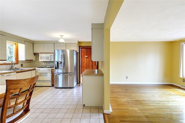 kitchen with white appliances, light tile patterned floors, baseboards, a sink, and backsplash