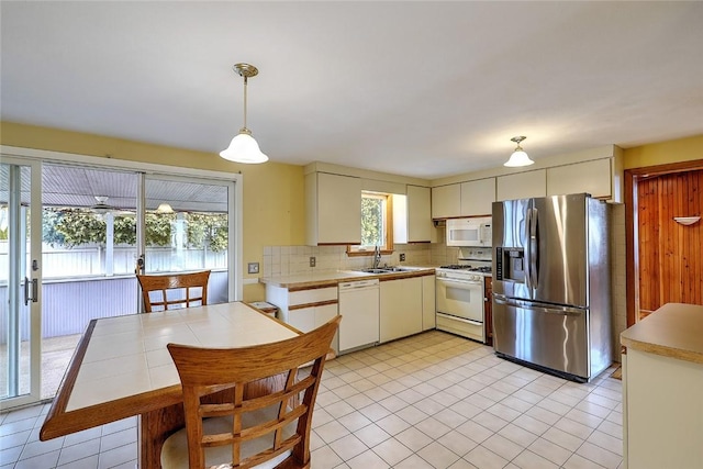 kitchen with backsplash, light countertops, hanging light fixtures, white appliances, and a sink